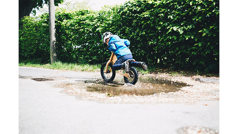 کودک روی دوچرخه با لباس آبی در چاله آب