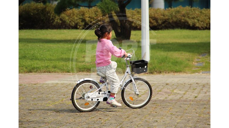 دختر بچه در حال دوچرخه سوار با دوچرخه دخترانه سفید
