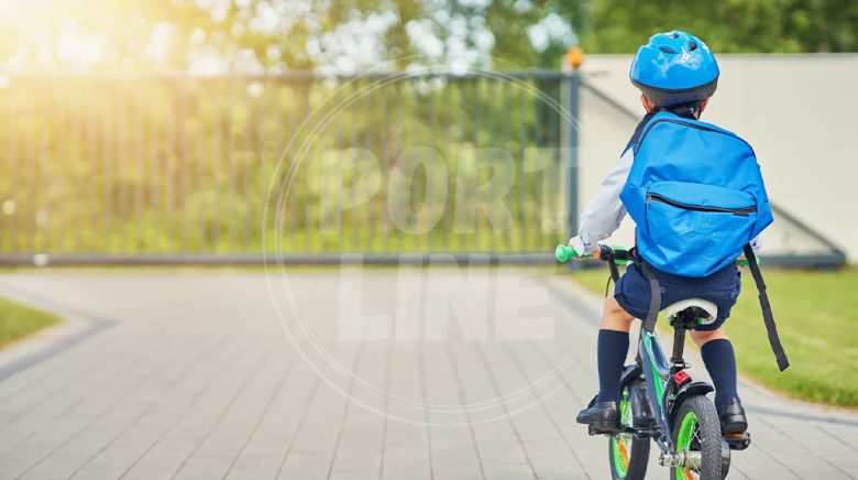 بچه مدرسه ای در حال رفتن به مدرسه با دوچرخه پسرانه و کوله پشتی آبی