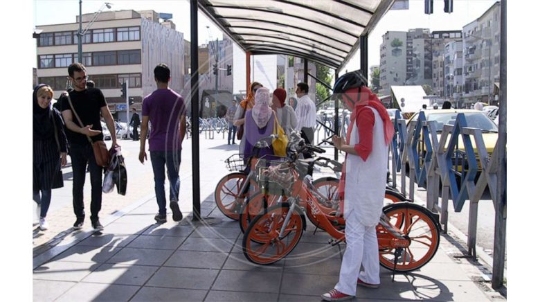 زن ایرانی در حال برداشتن دوچرخه اشتراکی